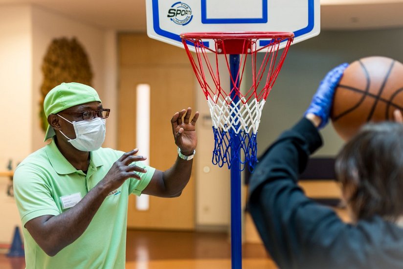 Ein Pflegehelfer spielt mit einem Klienten drinnen Basketball.