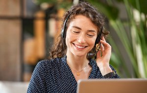 Eine Frau sitz an ihrem PC, sie trägt ein Headset telefoniert und lächelt dabei